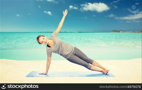 fitness, sport, people and healthy lifestyle concept - woman making yoga in side plank pose on mat over sea and sky background. woman making yoga in side plank pose on beach