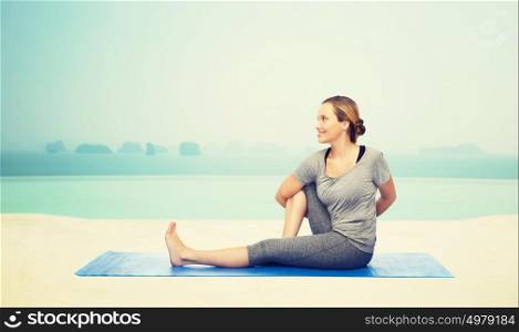 fitness, sport, people and healthy lifestyle concept - woman making yoga in twist pose on mat over infinity edge pool at hotel resort background. woman making yoga in twist pose on mat