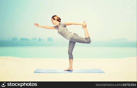 fitness, sport, people and healthy lifestyle concept - woman making yoga in lord of the dance pose on mat over infinity edge pool at hotel resort background. woman making yoga in lord of the dance pose on mat