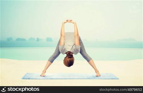 fitness, sport, people and healthy lifestyle concept - woman making yoga in wide-legged forward bend pose on mat over infinity edge pool at hotel resort background. woman making yoga wide-legged forward bend on mat