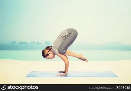 fitness, sport, people and healthy lifestyle concept - woman making yoga in crane pose on mat over infinity edge pool at hotel resort background. woman making yoga in crane pose on mat