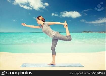 fitness, sport, people and healthy lifestyle concept - woman making yoga in lord of the dance pose on mat over sea and sky background. woman making yoga in lord of the dance pose