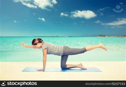 fitness, sport, people and healthy lifestyle concept - woman making yoga in balancing table pose on mat over beach background. woman making yoga in balancing table pose on mat