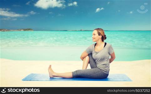 fitness, sport, people and healthy lifestyle concept - woman making yoga in twist pose on mat over sea and sky background. woman making yoga in twist pose on mat over beach