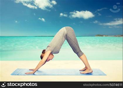 fitness, sport, people and healthy lifestyle concept - woman making yoga in downward facing dog pose on mat over beach background. woman making yoga dog pose on mat