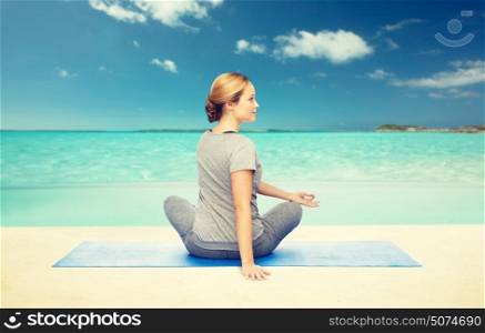 fitness, sport, people and healthy lifestyle concept - woman making yoga in twist pose on mat over beach background. woman making yoga in twist pose on mat