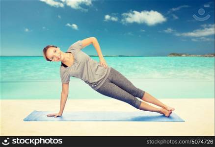 fitness, sport, people and healthy lifestyle concept - woman making yoga in side plank pose on mat over beach background. woman making yoga in side plank pose on mat