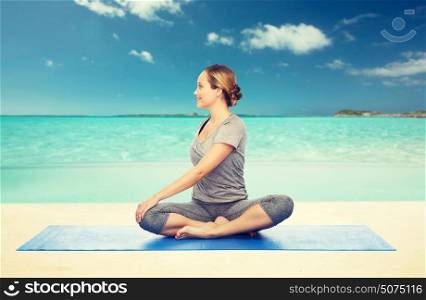 fitness, sport, people and healthy lifestyle concept - woman making yoga in twist pose on mat over beach background. woman making yoga in twist pose on mat