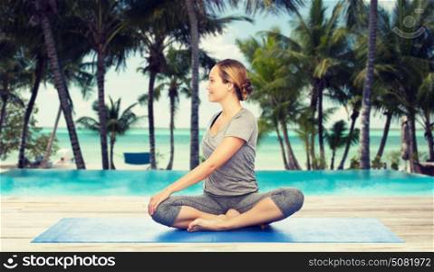 fitness, sport, people and healthy lifestyle concept - woman making yoga in twist pose on mat over hotel resort pool on tropical beach background. woman making yoga in twist pose on mat