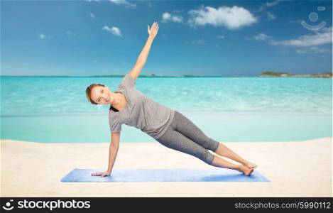 fitness, sport, people and healthy lifestyle concept - woman making yoga in side plank pose on mat over sea and sky background