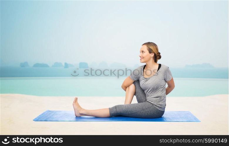fitness, sport, people and healthy lifestyle concept - woman making yoga in twist pose on mat over infinity edge pool at hotel resort background