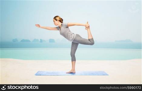 fitness, sport, people and healthy lifestyle concept - woman making yoga in lord of the dance pose on mat over infinity edge pool at hotel resort background