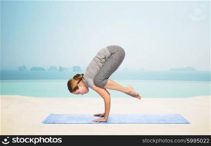 fitness, sport, people and healthy lifestyle concept - woman making yoga in crane pose on mat over infinity edge pool at hotel resort background
