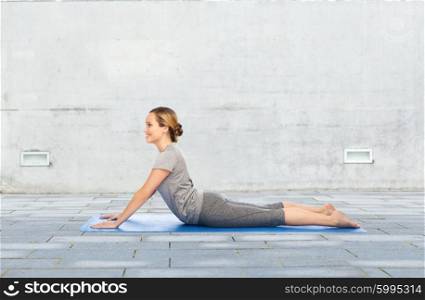 fitness, sport, people and healthy lifestyle concept - woman making yoga in dog pose on mat over urban street background