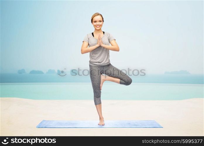 fitness, sport, people and healthy lifestyle concept - woman making yoga in tree pose on mat over infinity edge pool at hotel resort background