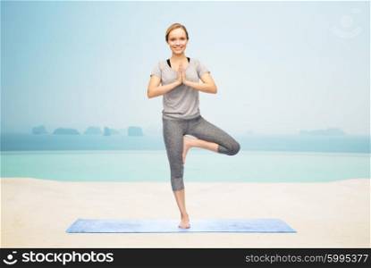 fitness, sport, people and healthy lifestyle concept - woman making yoga in tree pose on mat over infinity edge pool at hotel resort background