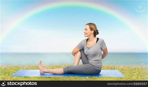 fitness, sport, people and healthy lifestyle concept - woman making yoga in twist pose on mat over blue sky, rainbow and sea background