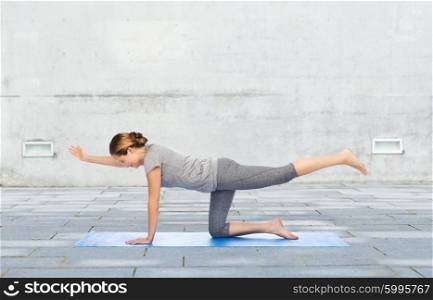 fitness, sport, people and healthy lifestyle concept - woman making yoga in balancing table pose on mat over urban street background