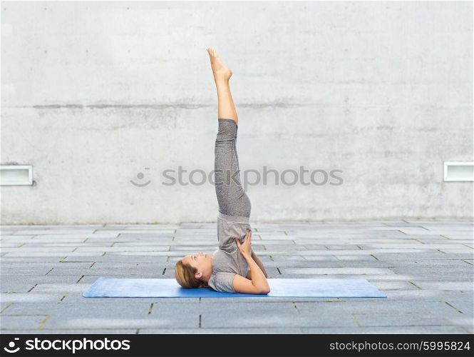 fitness, sport, people and healthy lifestyle concept - woman making yoga in shoulderstand pose on mat over urban street background