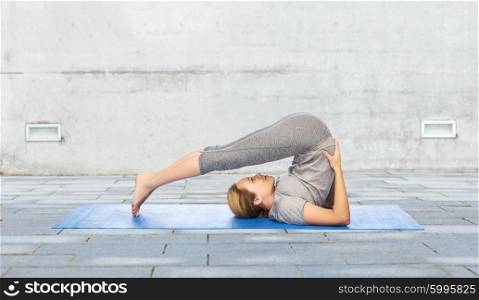 fitness, sport, people and healthy lifestyle concept - woman making yoga in plow pose on mat over urban street background