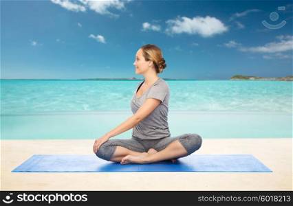 fitness, sport, people and healthy lifestyle concept - woman making yoga in twist pose on mat over beach background