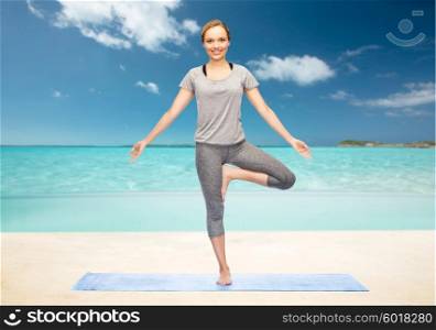 fitness, sport, people and healthy lifestyle concept - woman making yoga in tree pose on mat over beach background