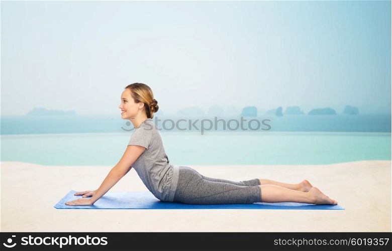 fitness, sport, people and healthy lifestyle concept - woman making yoga in dog pose on mat over infinity edge pool at hotel resort background