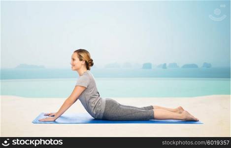 fitness, sport, people and healthy lifestyle concept - woman making yoga in dog pose on mat over infinity edge pool at hotel resort background