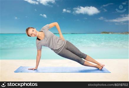 fitness, sport, people and healthy lifestyle concept - woman making yoga in side plank pose on mat over beach background