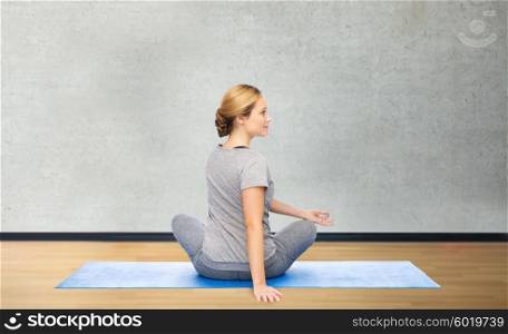 fitness, sport, people and healthy lifestyle concept - woman making yoga in twist pose on mat over gym room background