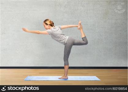 fitness, sport, people and healthy lifestyle concept - woman making yoga in lord of the dance pose on mat over gym room background