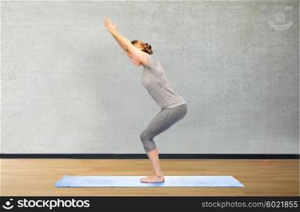fitness, sport, people and healthy lifestyle concept - woman making yoga in chair pose on mat over gym room background