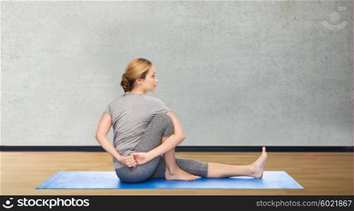 fitness, sport, people and healthy lifestyle concept - woman making yoga in twist pose on mat over gym room background