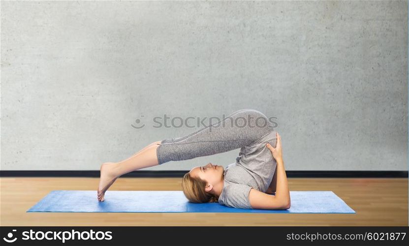 fitness, sport, people and healthy lifestyle concept - woman making yoga in plow pose on mat over gym room background