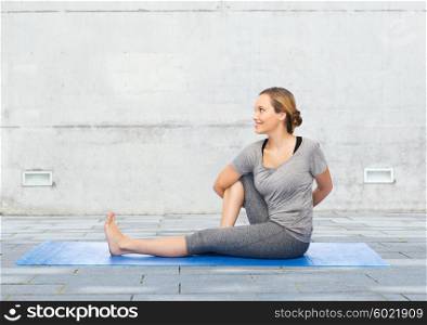 fitness, sport, people and healthy lifestyle concept - woman making yoga in twist pose on mat over urban street background