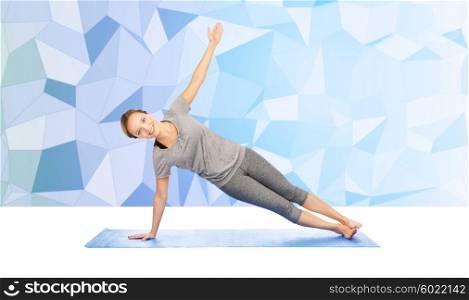 fitness, sport, people and healthy lifestyle concept - woman making yoga in side plank pose on mat over blue polygonal background