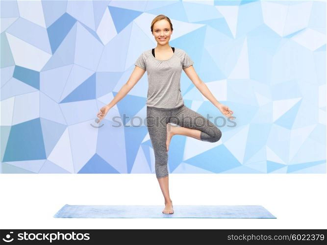fitness, sport, people and healthy lifestyle concept - woman making yoga in tree pose on mat over low poly background