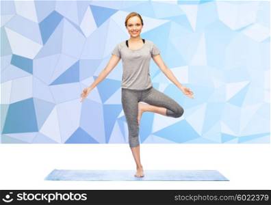 fitness, sport, people and healthy lifestyle concept - woman making yoga in tree pose on mat over low poly background