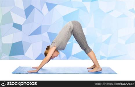 fitness, sport, people and healthy lifestyle concept - woman making yoga in downward facing dog pose on mat over low poly background