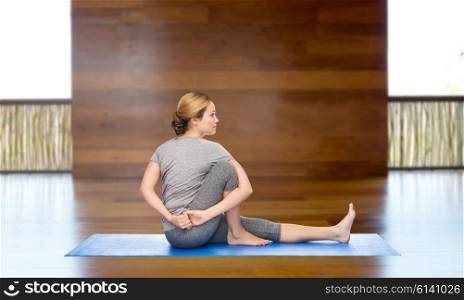 fitness, sport, people and healthy lifestyle concept - woman making yoga in twist pose on mat over wooden gym background