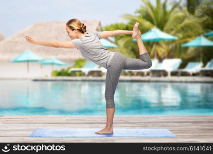 fitness, sport, people and healthy lifestyle concept - woman making yoga in lord of the dance pose on mat over beach and swimming pool background
