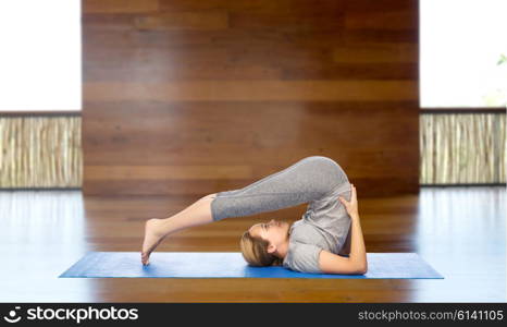 fitness, sport, people and healthy lifestyle concept - woman making yoga in plow pose on mat over wooden gym background