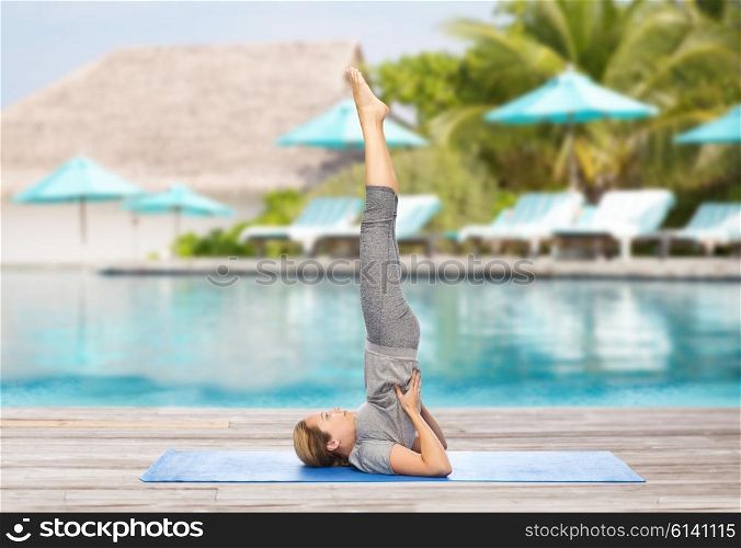 fitness, sport, people and healthy lifestyle concept - woman making yoga in shoulderstand pose on mat over beach and swimming pool background