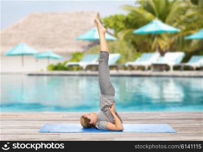fitness, sport, people and healthy lifestyle concept - woman making yoga in shoulderstand pose on mat over beach and swimming pool background