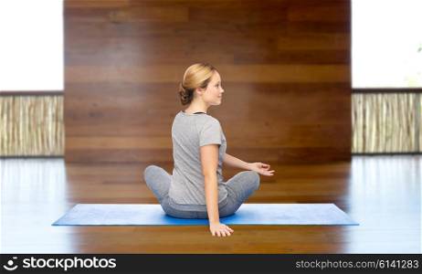 fitness, sport, people and healthy lifestyle concept - woman making yoga in twist pose on mat over wooden gym background