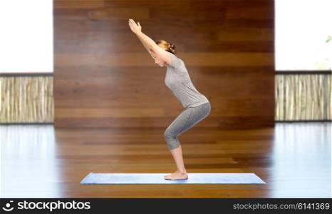 fitness, sport, people and healthy lifestyle concept - woman making yoga in chair pose on mat over wooden gym background