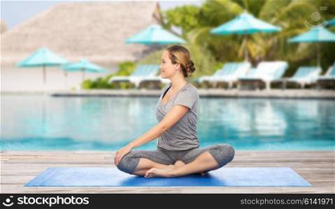 fitness, sport, people and healthy lifestyle concept - woman making yoga in twist pose on mat over beach and swimming pool background