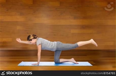 fitness, sport, people and healthy lifestyle concept - woman making yoga in balancing table pose on mat over wooden room background
