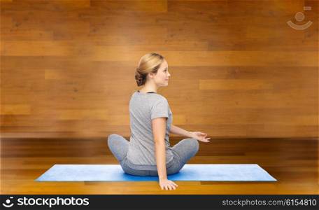 fitness, sport, people and healthy lifestyle concept - woman making yoga in twist pose on mat over wooden room background