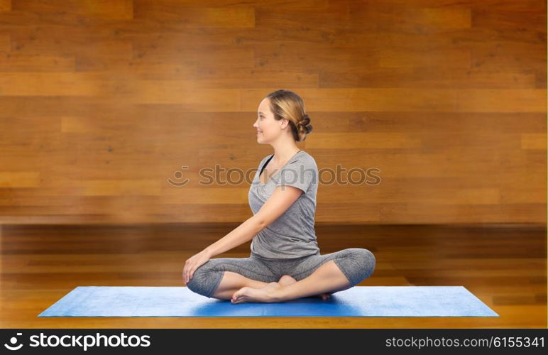 fitness, sport, people and healthy lifestyle concept - woman making yoga in twist pose on mat over wooden room background